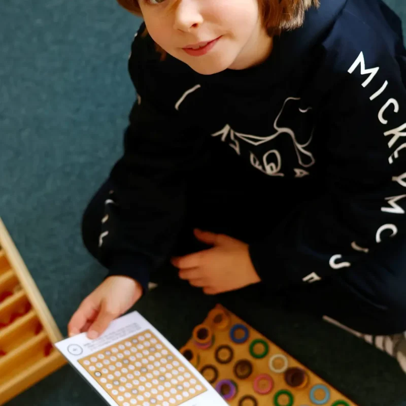 Kind nutzt ein Montessori-Farb- und Formenmaterial und sortiert die Plättchen.