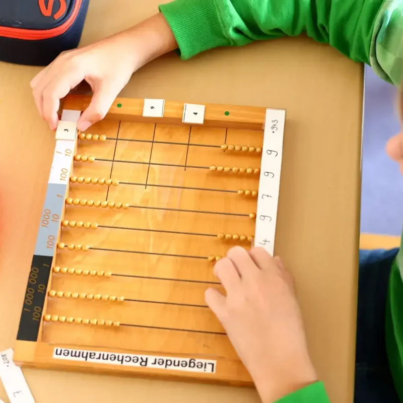 Kind arbeitet mit einem Montessori-Rechenrahmen und legt Zahlenstäbe aus.