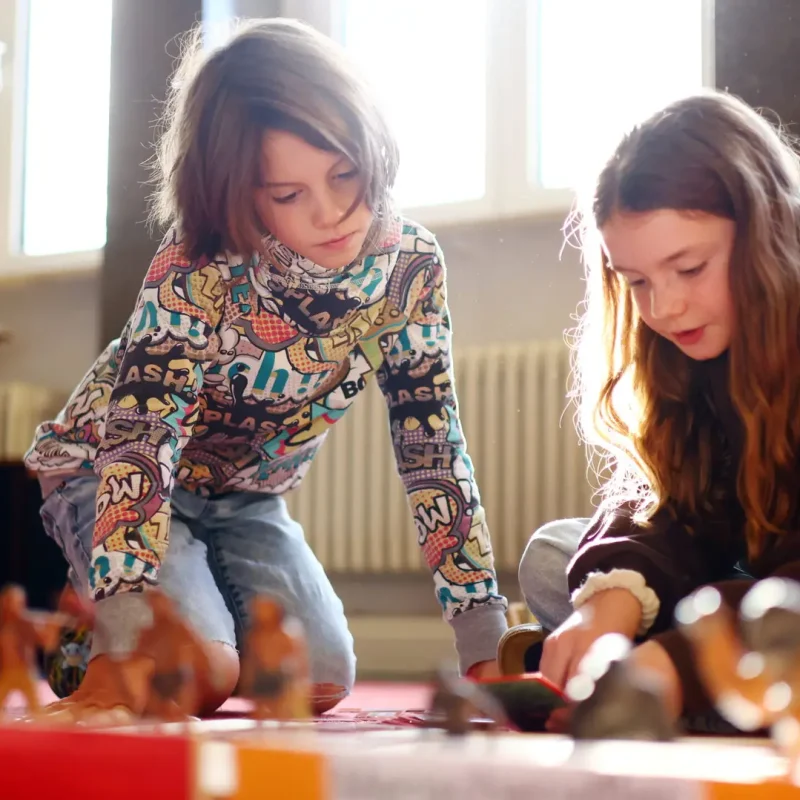 Zwei Mädchen arbeiten gemeinsam an einem Montessori-Wissensspiel und tauschen sich aus.