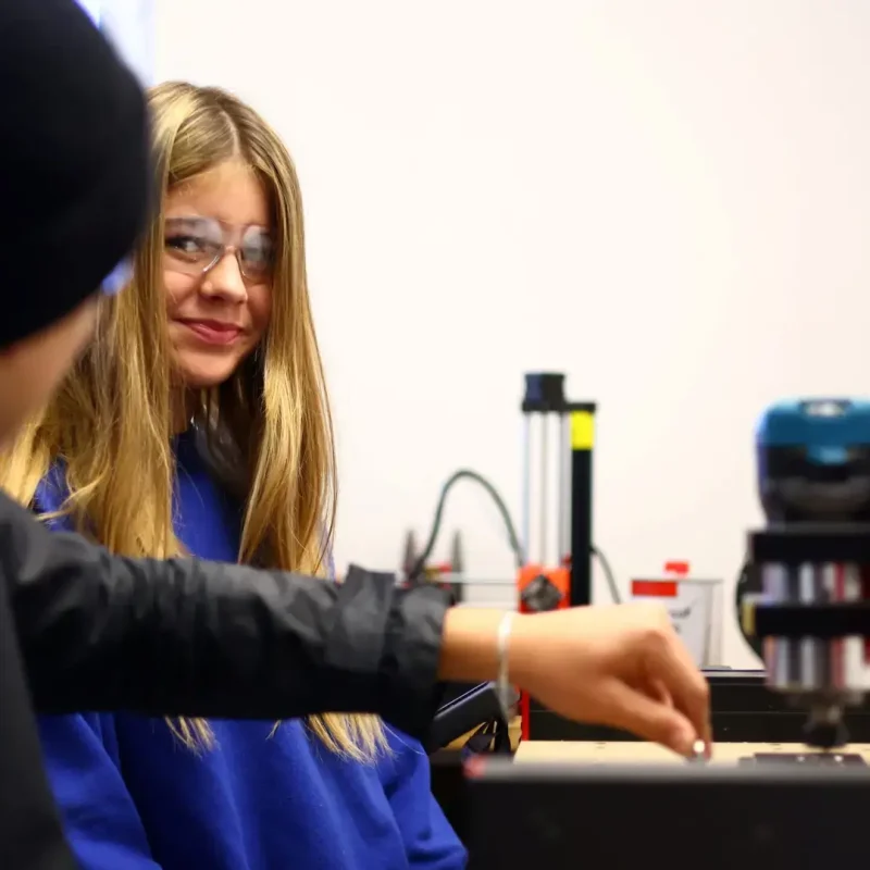 Schülerin im Technikraum misst ein Bauteil und arbeitet konzentriert an einem Projekt.