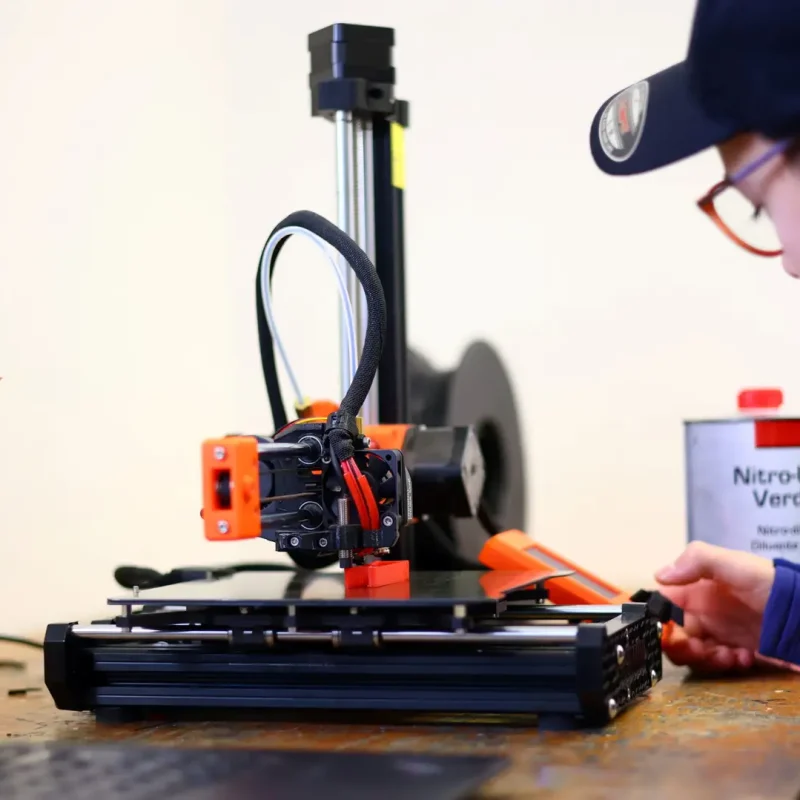 3D-Drucker druckt ein orangefarbenes Bauteil für den Technikunterricht.