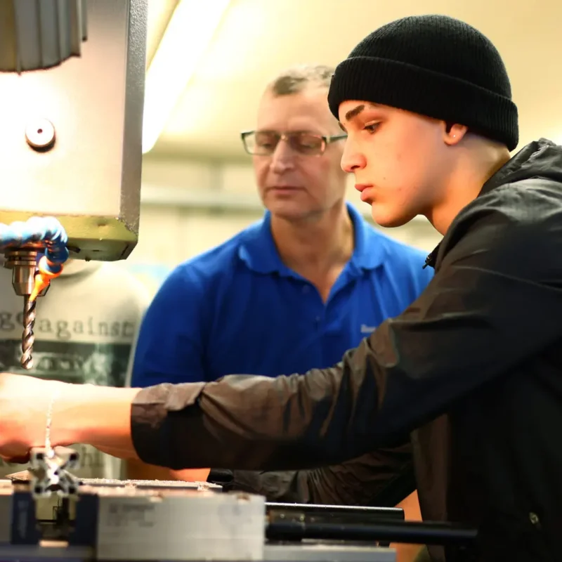 Jugendliche arbeiten mit Metallwerkzeugen an einem technischen Projekt in der Werkstatt.