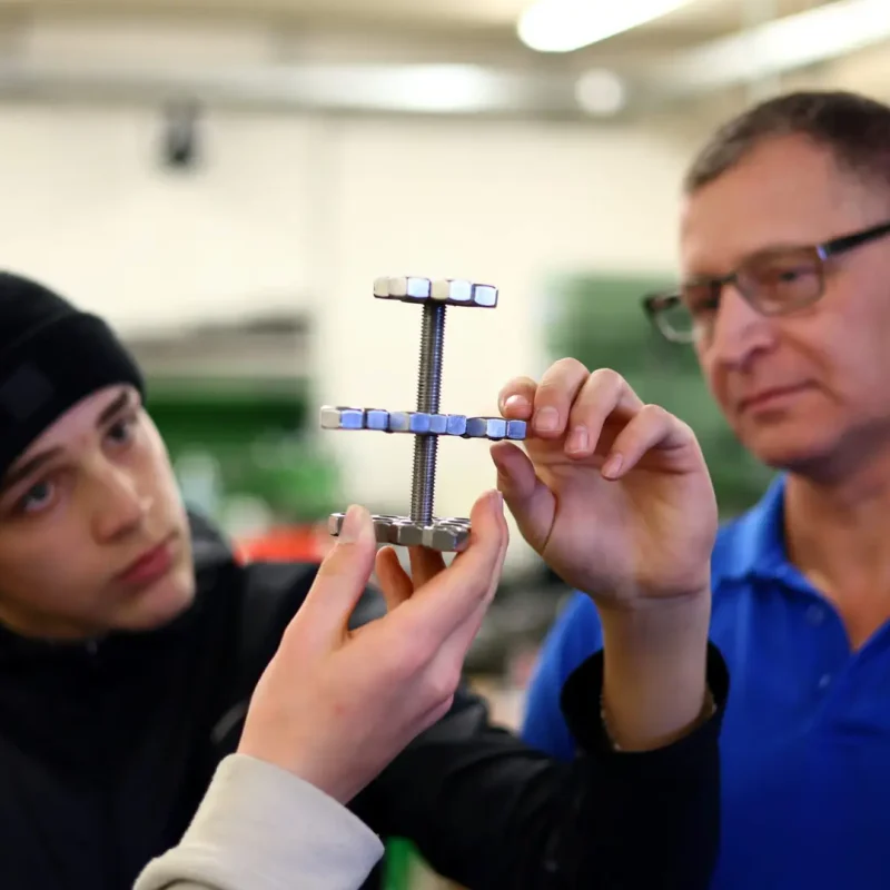 Lehrkraft und Schüler halten ein Werkstück und prüfen die richtige Ausrichtung.