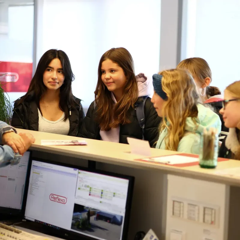 Gruppe Jugendlicher informiert sich an einem Empfangstresen über ein schulisches Angebot.