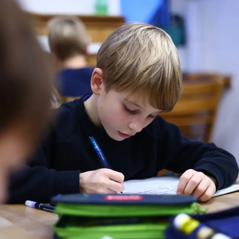 Junge schreibt fokussiert in sein Heft während einer Montessori-Arbeitsphase.