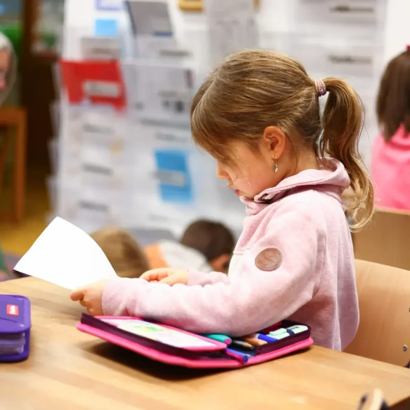 Kind schreibt im Klassenzimmer und arbeitet mit seinem Federmäppchen.