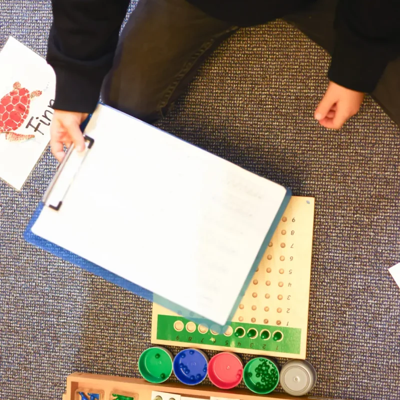 Kind arbeitet am Boden mit Montessori-Materialien und einem großen Ziffernfeld.