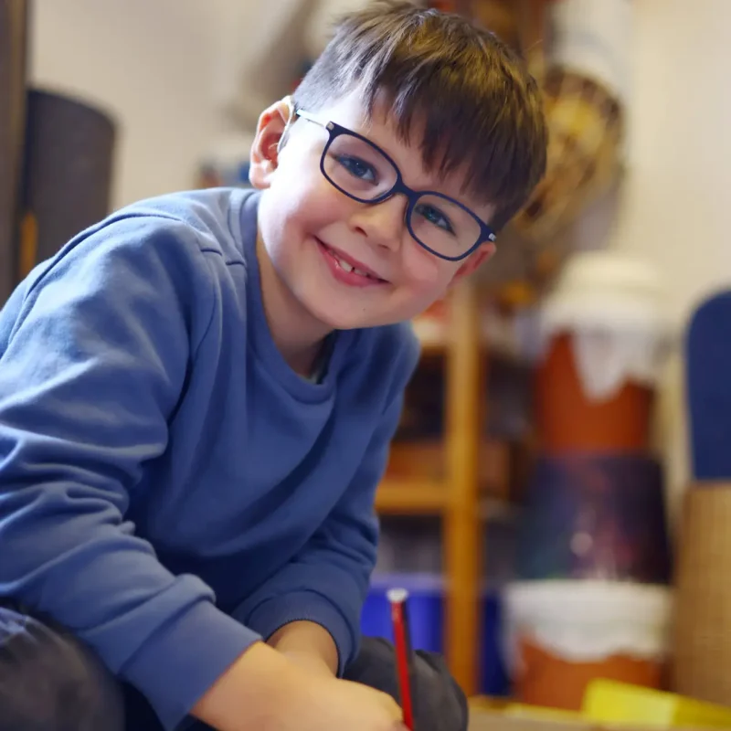 Junge lächelt in die Kamera, während er an einer Aufgabe arbeitet.