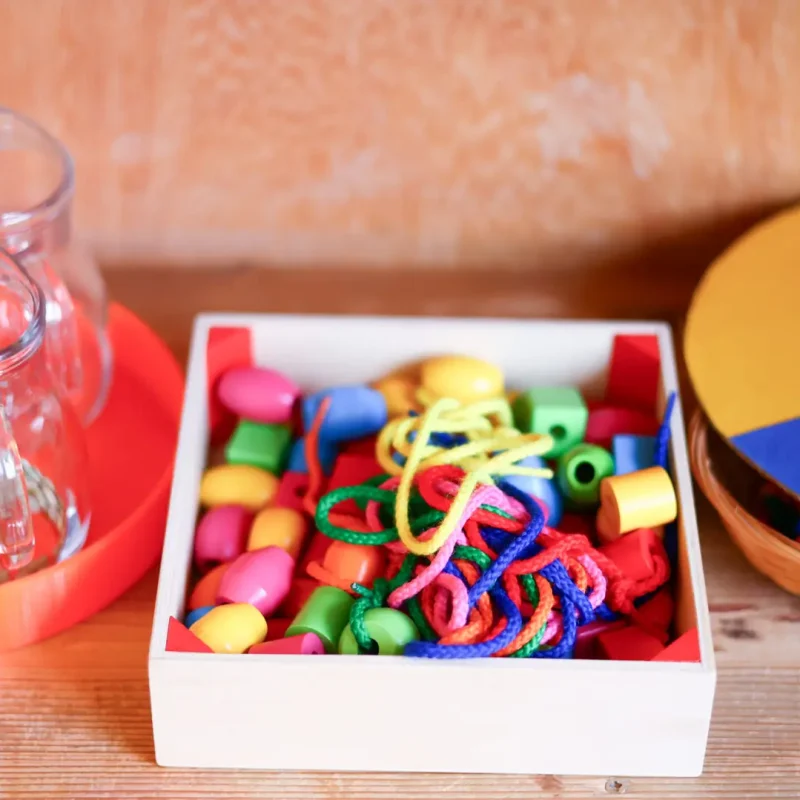 Box mit bunten Bastelmaterialien wie Perlen, Ringen und Holzstücken für kreative Freiarbeit.