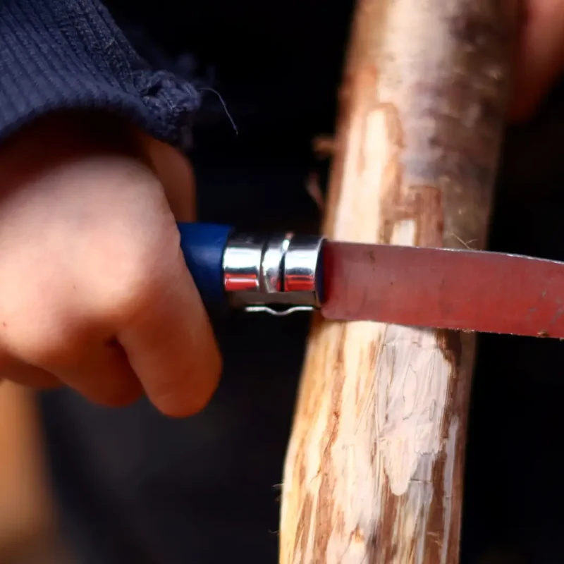 Nahaufnahme der Kinderhände beim Feilen und Bearbeiten eines Holzstocks.